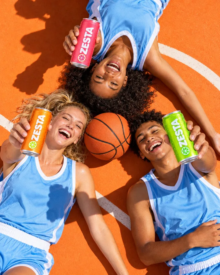 Three basketball players lying on an orange court holding cans