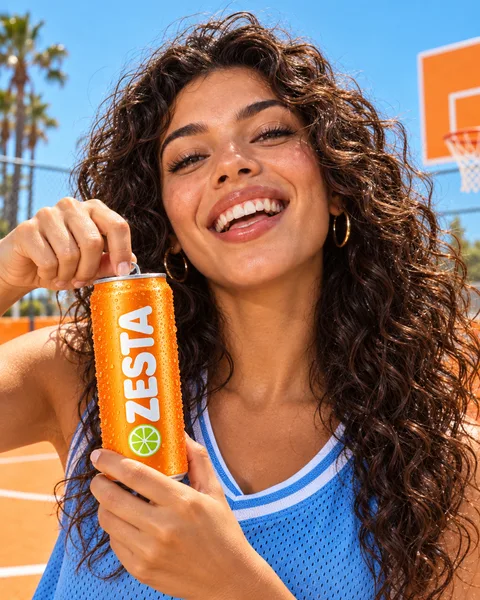 A woman about to open a ZESTA can on an orange court